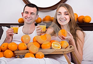 Man and girlfriend drinking squeezed orange juice in bed