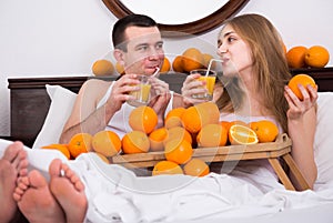 Man and girlfriend drinking squeezed orange juice in bed