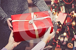 Man is giving a big red gift box to a woman against amazing christmas tree background. Toned and selective focus