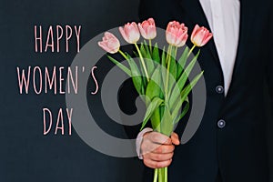 Man giving a bouquet of pink flowers tulips. Greeting card with text Happy Women`s Day