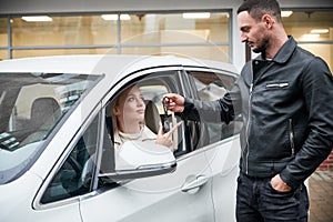 Man giving car keys to girl driving auto.