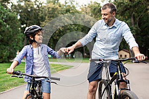 Man giving fist bump to son riding bicycles at park