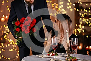 Man giving flowers to his girlfriend during romantic date in restaurant