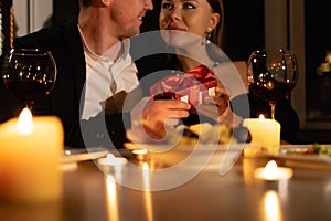 Man giving a gift to a woman on a date, romantic candlelight dinner for two, wedding anniversary with wine in a