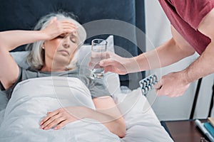 Man giving glass of water and pills to sick wife