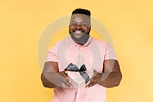 Man giving heart shaped gift box to camera with excited smile, greeting on holiday, sharing present.