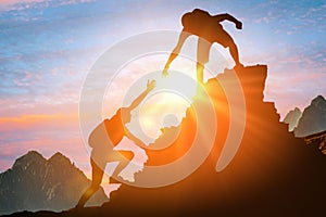 Man is giving helping hand. Silhouettes of people climbing on mountain at sunset. Help and assistance concept. Silhouettes of two