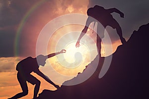 Man is giving helping hand. Silhouettes of people climbing on mountain at sunset photo