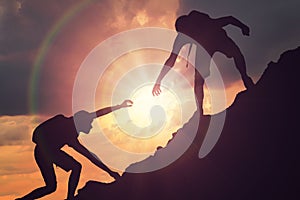 Man is giving helping hand. Silhouettes of people climbing on mountain at sunset