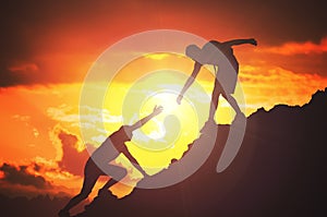 Man is giving helping hand. Silhouettes of people climbing on mountain at sunset photo