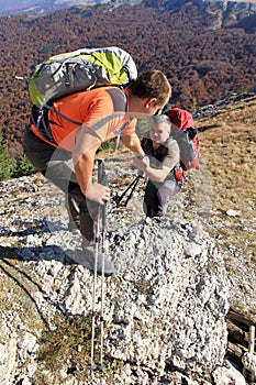 Man giving helping hand to friend to climb mountain rock cliff.