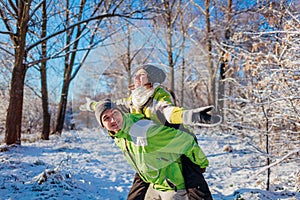 Man giving his girlfriend piggyback in winter forest. Couple in love having fun