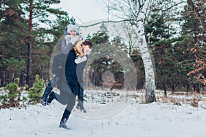 Man giving his girlfriend piggyback in winter forest. Couple in love having fun outdoors. Winter activities