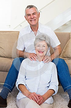 Man giving his relaxed senior wife a shoulder rub smiling at camera