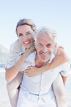 Man giving his smiling wife a piggy back at the beach