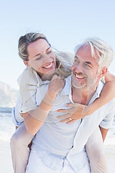 Man giving his smiling wife a piggy back at the beach