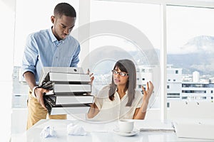 Man giving pile of files to his exasperated colleague