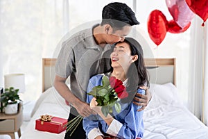 Man giving a rose and a kiss to his beautiful wife in bed Valentine's Day concept