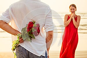 Man giving roses to his surprise and wonder woman on the ocean beach. romantic date or wedding or valentines day concept