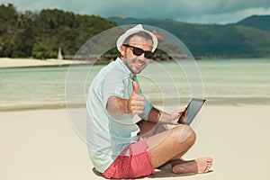 Man giving thumbs up while sitting on the beach with ipad