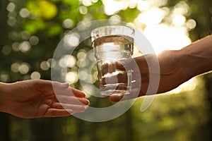 Man giving woman glass of fresh water in forest on sunny day, closeup