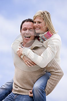 Man giving woman piggyback ride outdoors smiling