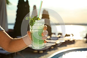 Man with glass of fresh summer cocktail near swimming pool outdoors at sunset. Space for text