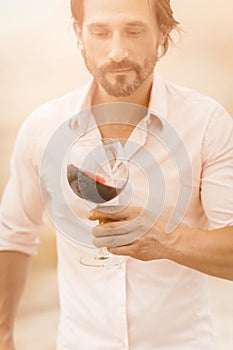 Man with glass of red wine. Bearded caucasian man in a white shirt holds a glass of red wine looking on it. Winetasting