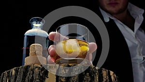 A man with a glass of whiskey in his hands. Whiskey with ice on a black background on a wooden board