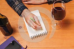 Man with a glass of wine writing in his notepad, tracking amount of alcohol or making notes