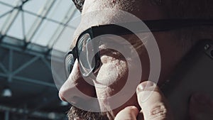 Man with glasses and beard speaks on the phone: close-up of profile