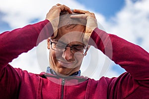 A man in glasses desperately holds his head.