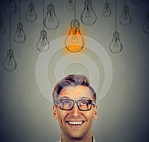 Man in glasses looking up at bright idea light bulb above head