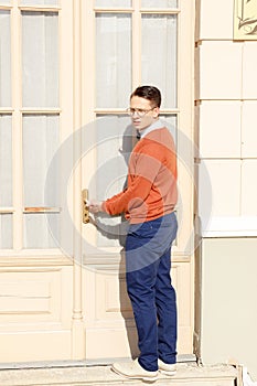 Man with glasses in the orange sweater trying to open the door