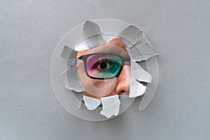 Man in glasses peeping through hole on paper