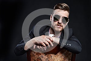 Man in glasses sits on a chair. Businessman confident man. SEO Manager posing on a black background. Successful entrepreneur.