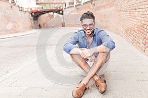 Man with glasses sitting on the sidewalk in a city