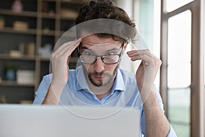 Man in glasses stare wide-eyed at laptop screen