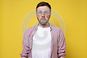 Man with glasses in a stupor stands motionless, he is frightened and shocked. Yellow background.