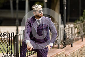 Man in glasses and violet luxery three-piece suit, bow tie posing on the street