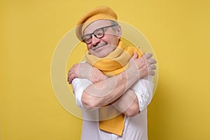 Man in glasses and yellow hat and scarf hugs himself, has high self esteem