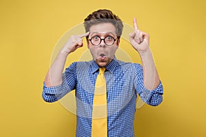 Man in glasses yellow tie and blue shirt has intriguing expression pointing finger up having great idea looks happily