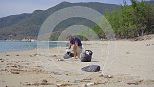 Man in gloves collects plastic trash on a beach. The problem of garbage on the beach sand caused by man-made pollution