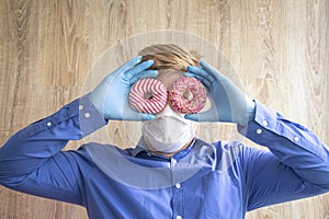 Man in gloves and mask holds donuts like glasses