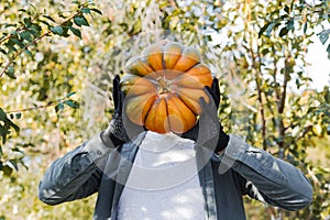 Man in glovs holds a yellow pumpkin instead of a head at outdoor farmer market. Funny pumpkin. A field in autumn harvest time.