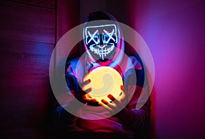 Man in glowing mask sitting in the corner with moon-shaped lamp