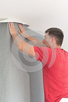 A man glues vinyl wallpaper on the wall, repairs in the room and wallpapering.