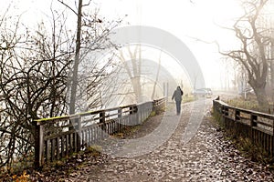 The man goes along the bridge in the fog to the car