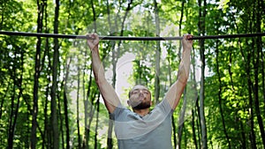 Man goes in for sports doing pull-up exercises on horizontal bar outside. Male