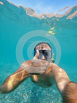 Man in goggles and fins swims under water with his thumb up